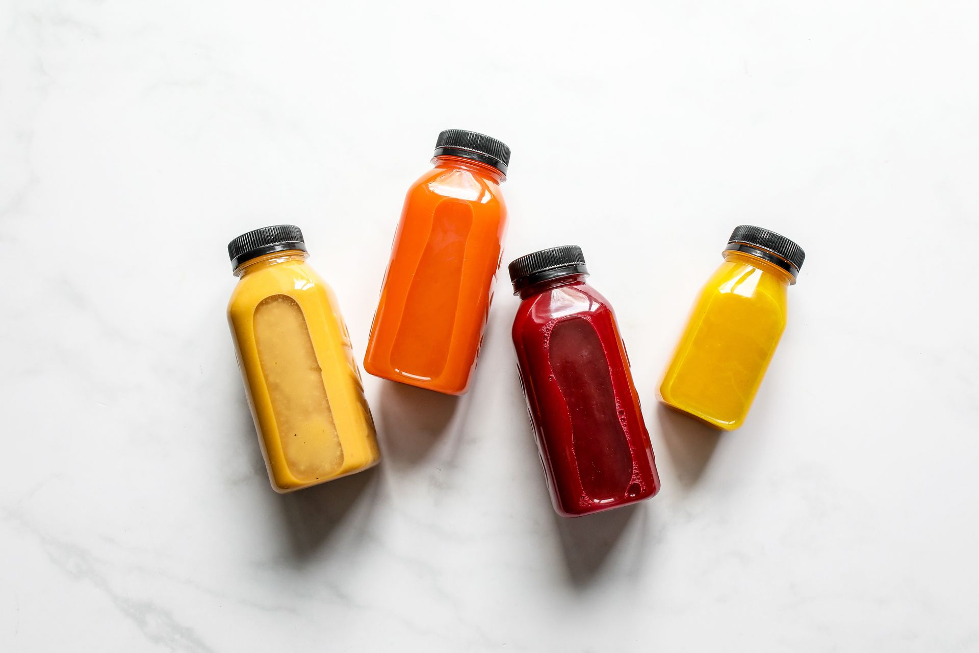Four bottles of cold-pressed juice on white marble