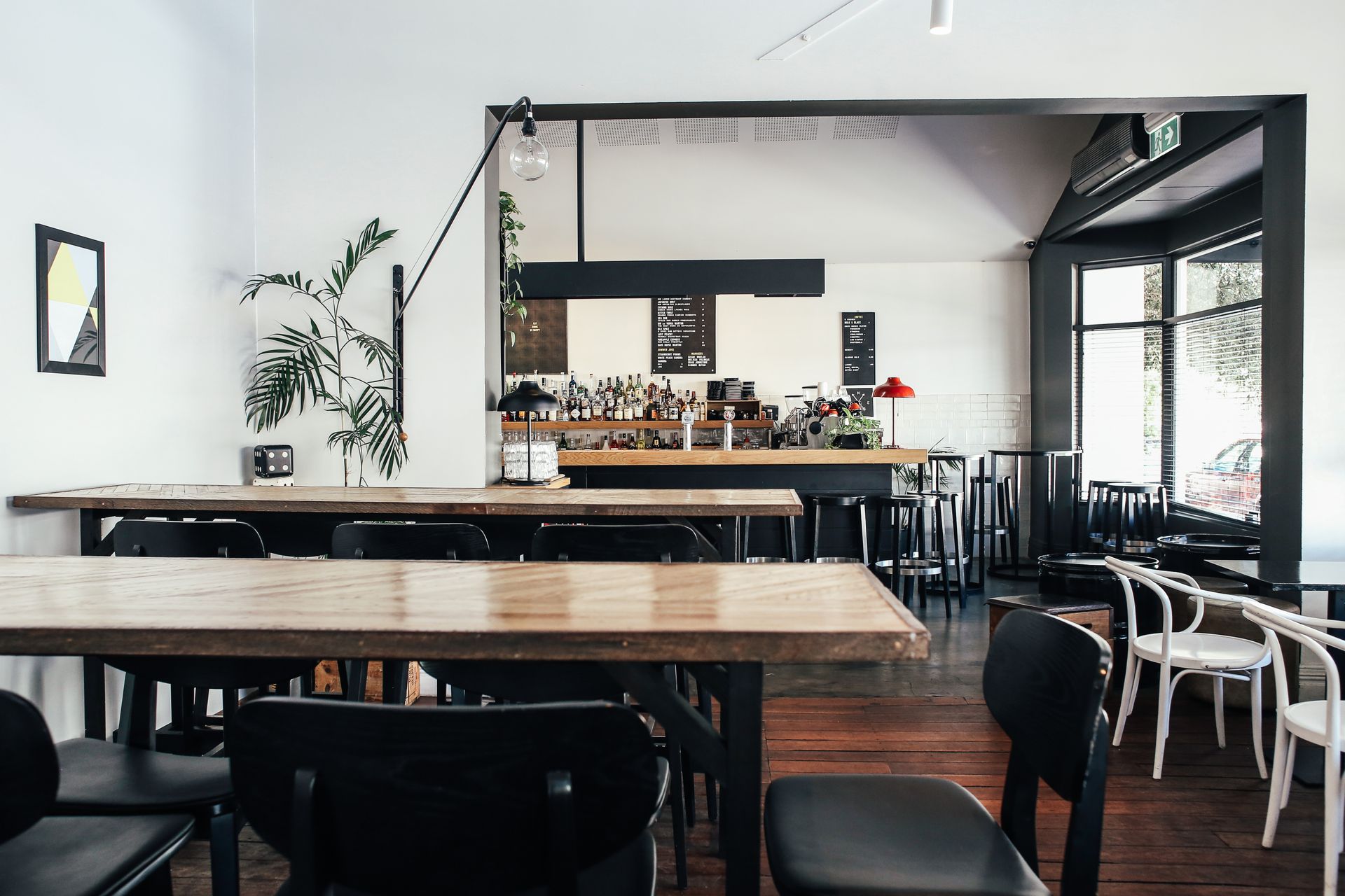 A white-walled cafe with long wooden tables and a bar at the back