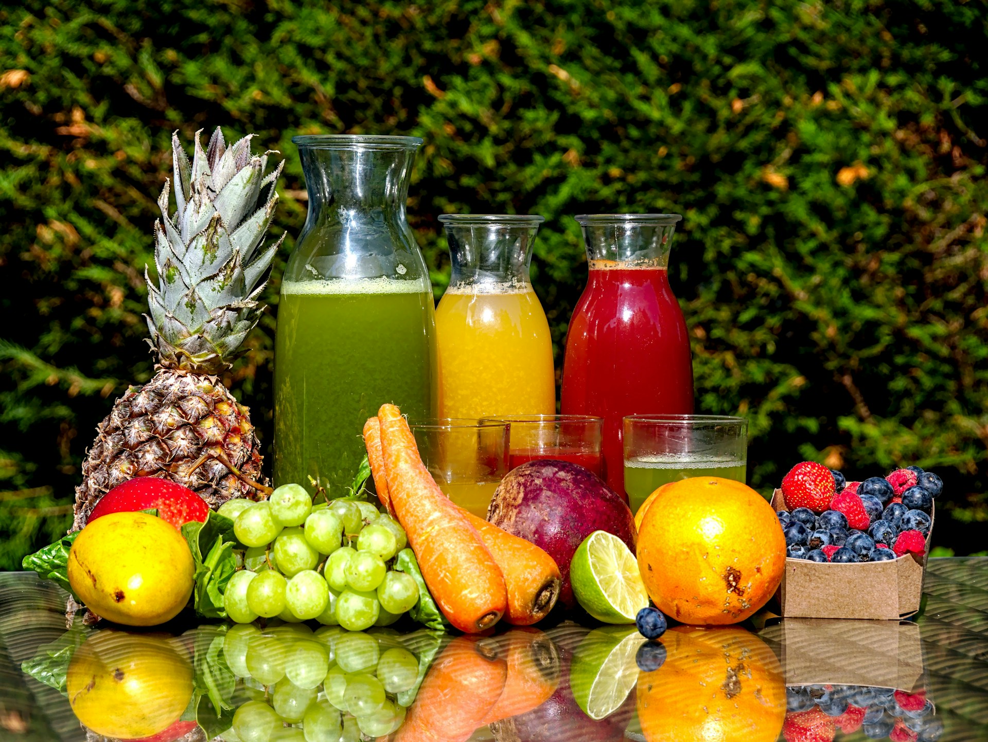 Fresh juices in glass carafes beside pineapple, carrots, grapes, citrus and berries