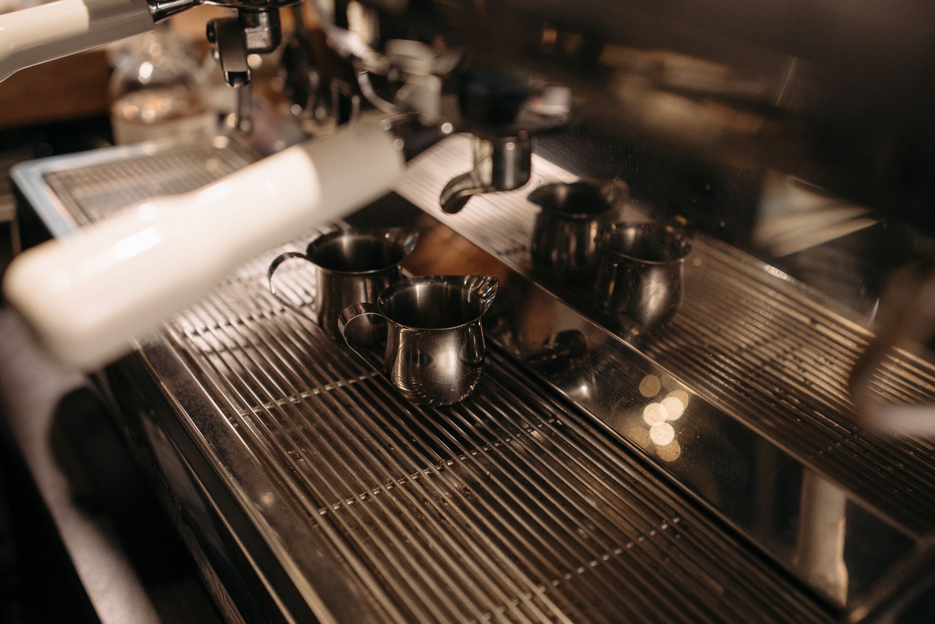 Steel milk pitchers resting on an espresso machine